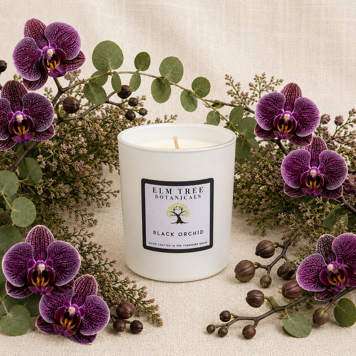White candle with 'Elm Tree Botanicals' label surrounded by purple orchids and green leaves on a beige background