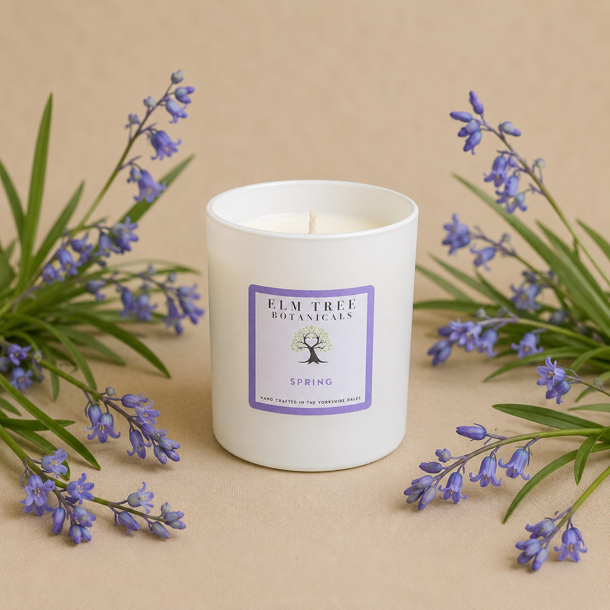 White candle with a purple label surrounded by lavender flowers on a beige background
